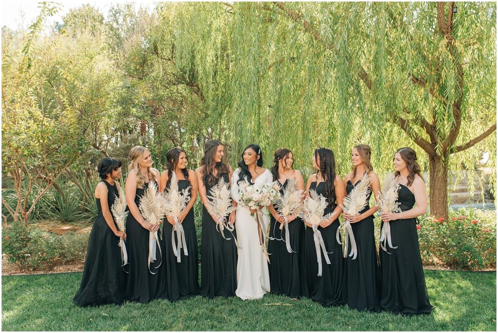 bride holding white bouquet with anemones, bridesmaids wearing black dresses and holding dried pampas grass bouquets